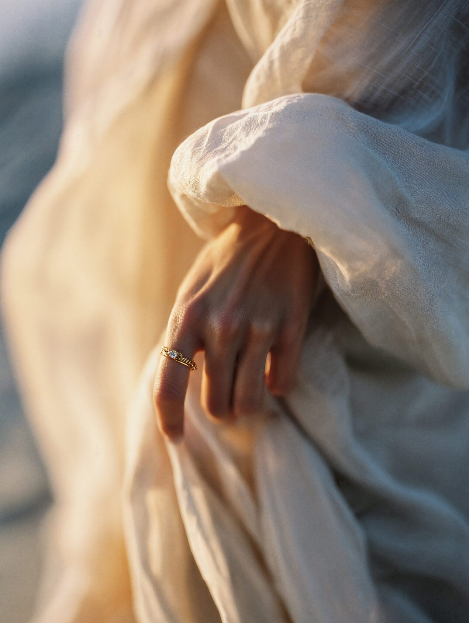 Photoreal macro of golden engagement ring on fabric in warm sunlight, luxury jewelry campaign still