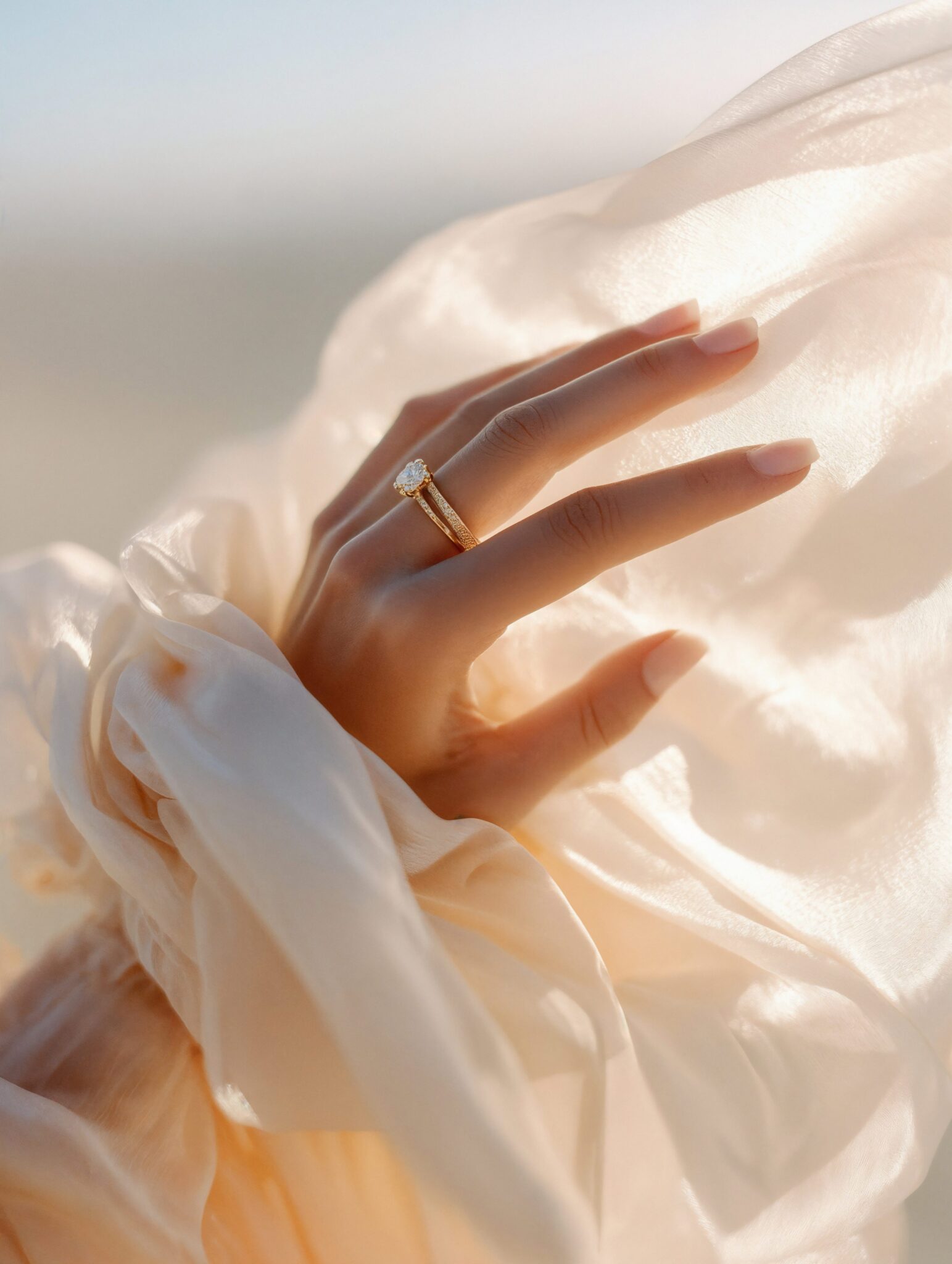 Photoreal AI macro of engagement ring on hand in flowing fabric, cinematic golden light, luxury jewelry still